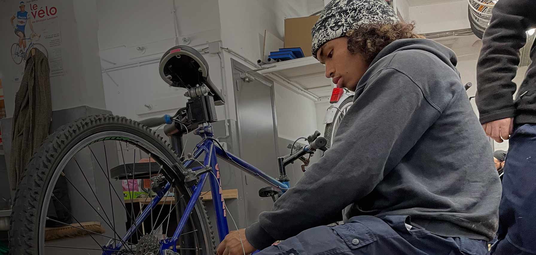 Jeune homme assis qui répare un vélo dans un atelier
